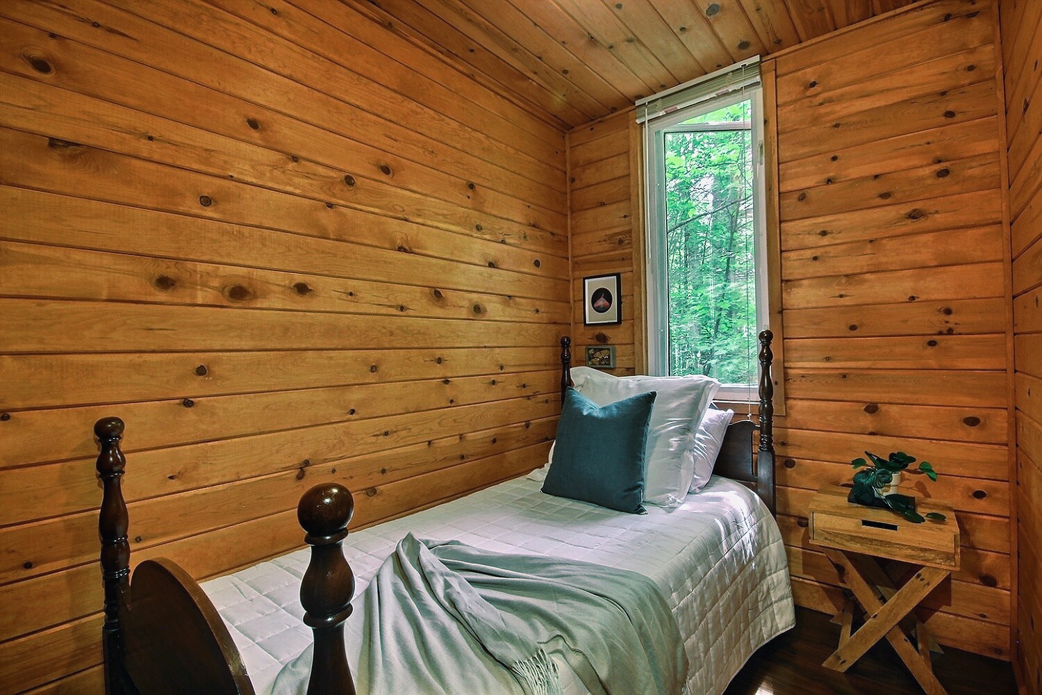 A small white bed with a green blanket pressed against a wall in a wood panelled room