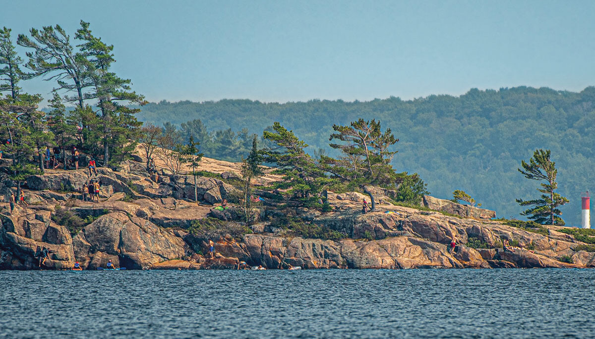 A section of Canadian Shield rocks along a lake, with people jumping off to swim
