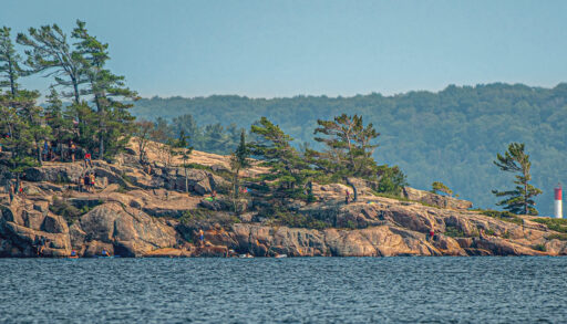 A section of Canadian Shield rocks along a lake, with people jumping off to swim