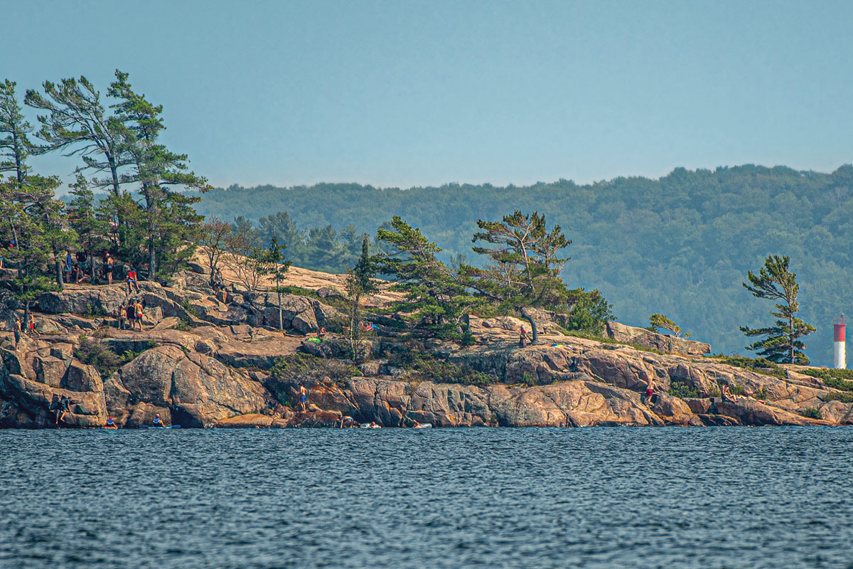 A section of Canadian Shield rocks along a lake, with people jumping off to swim