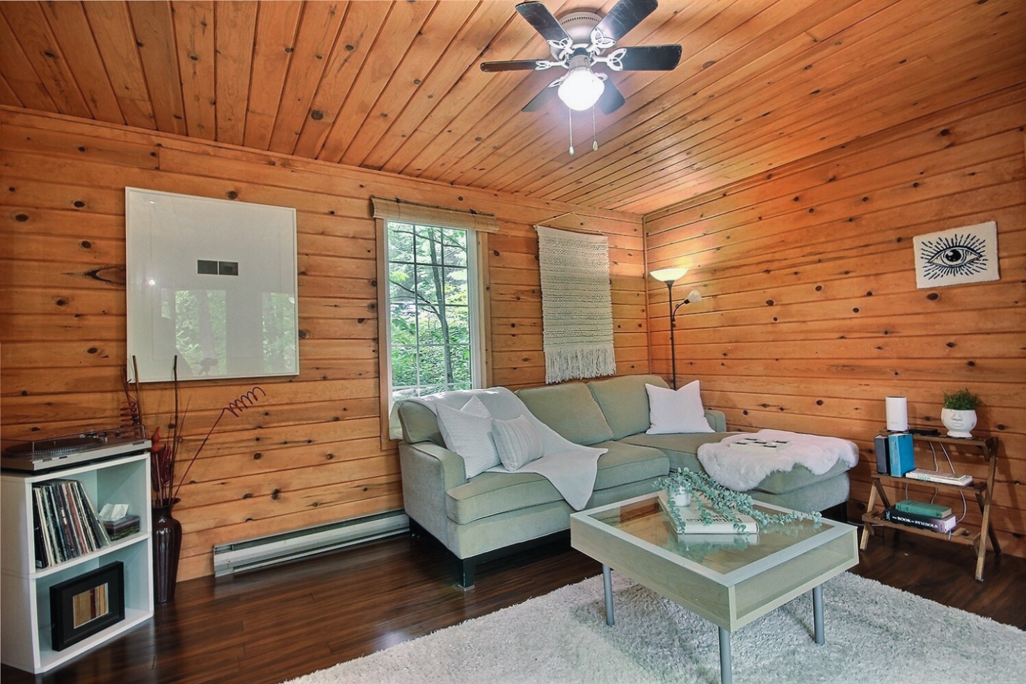 A white couch in the corner of a wood panelled room faces a white coffee table