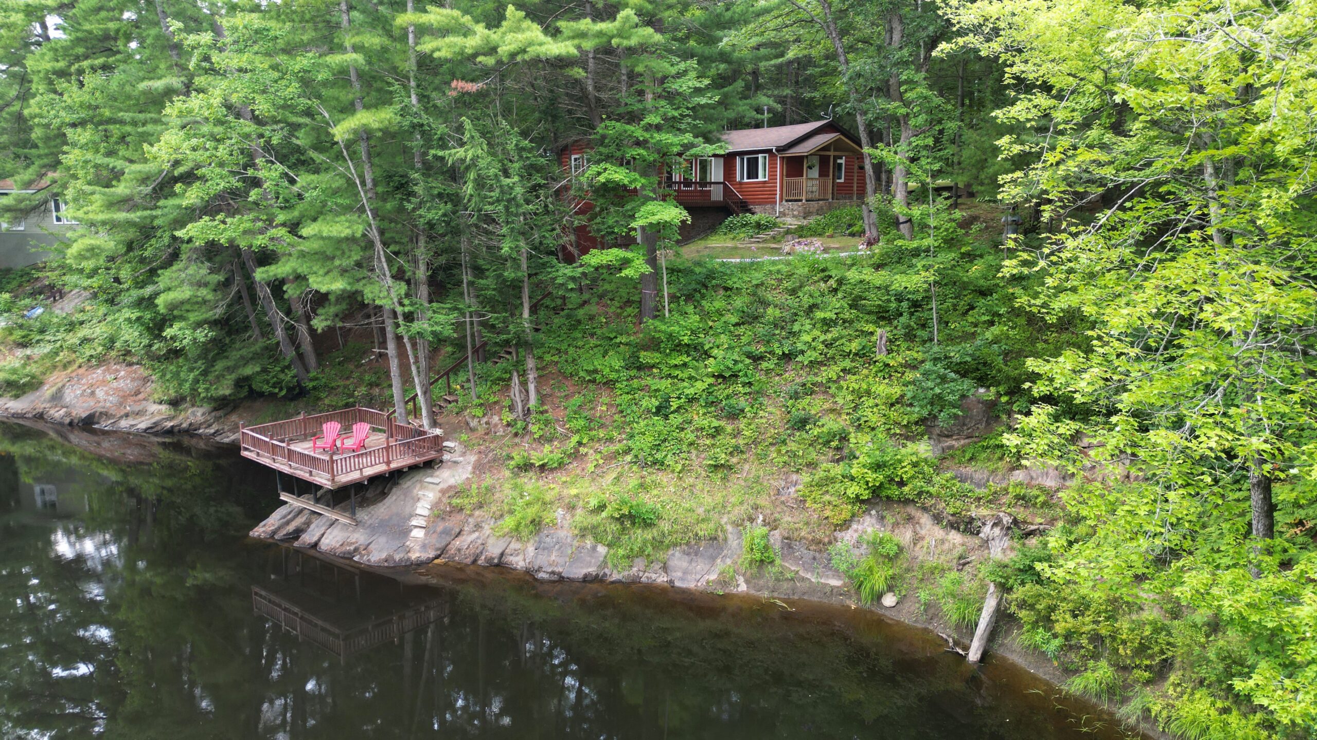Aerial view of a red cottage hidden amongst green trees near a brown river