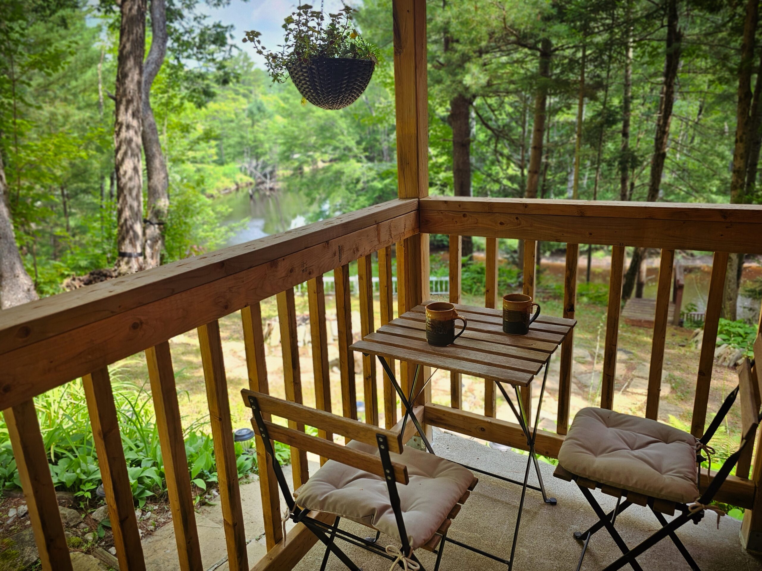A small seating area on a wood deck faces green trees