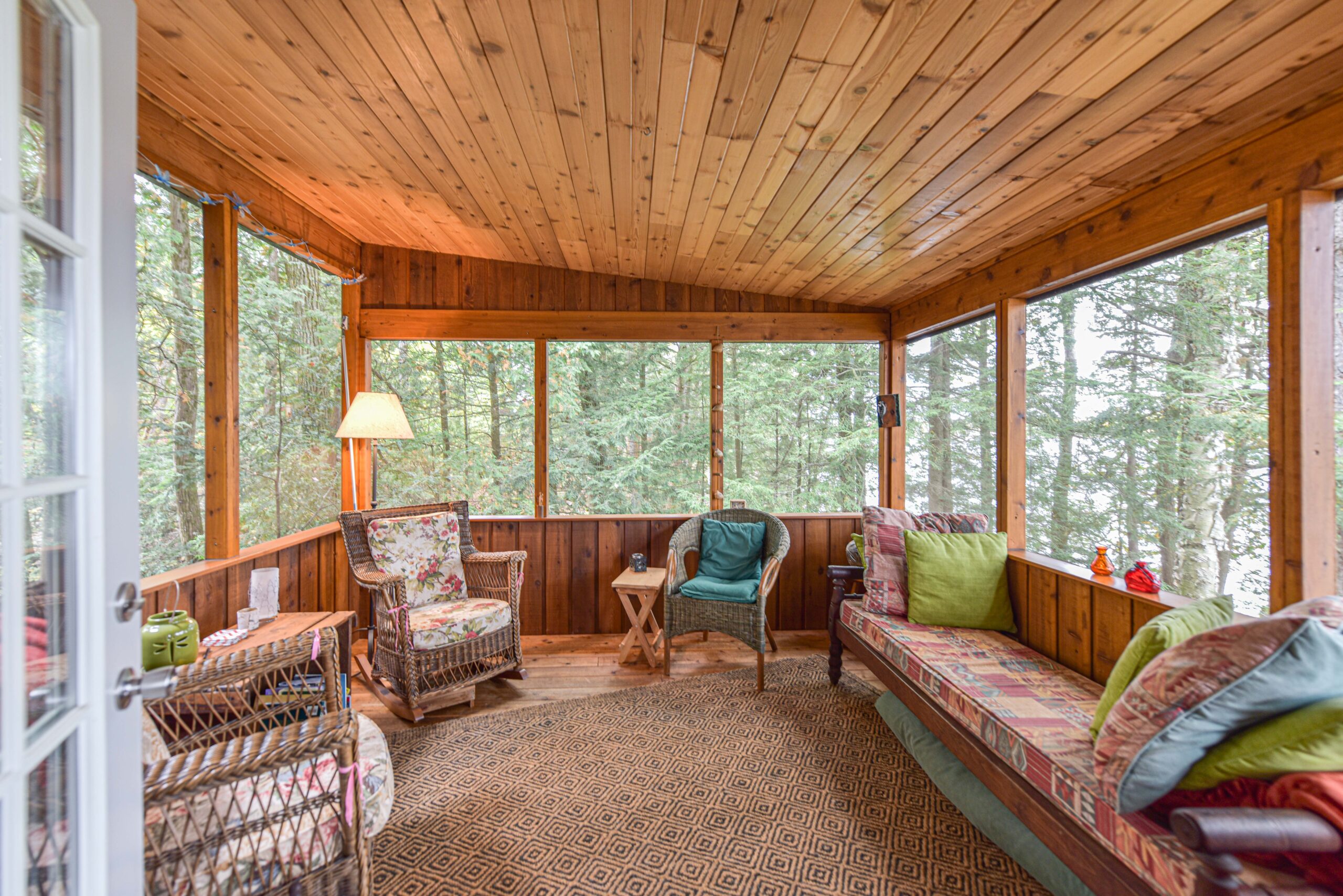 Wicker chairs and a long patterned couch in a bright sun room with a wood panelled ceiling