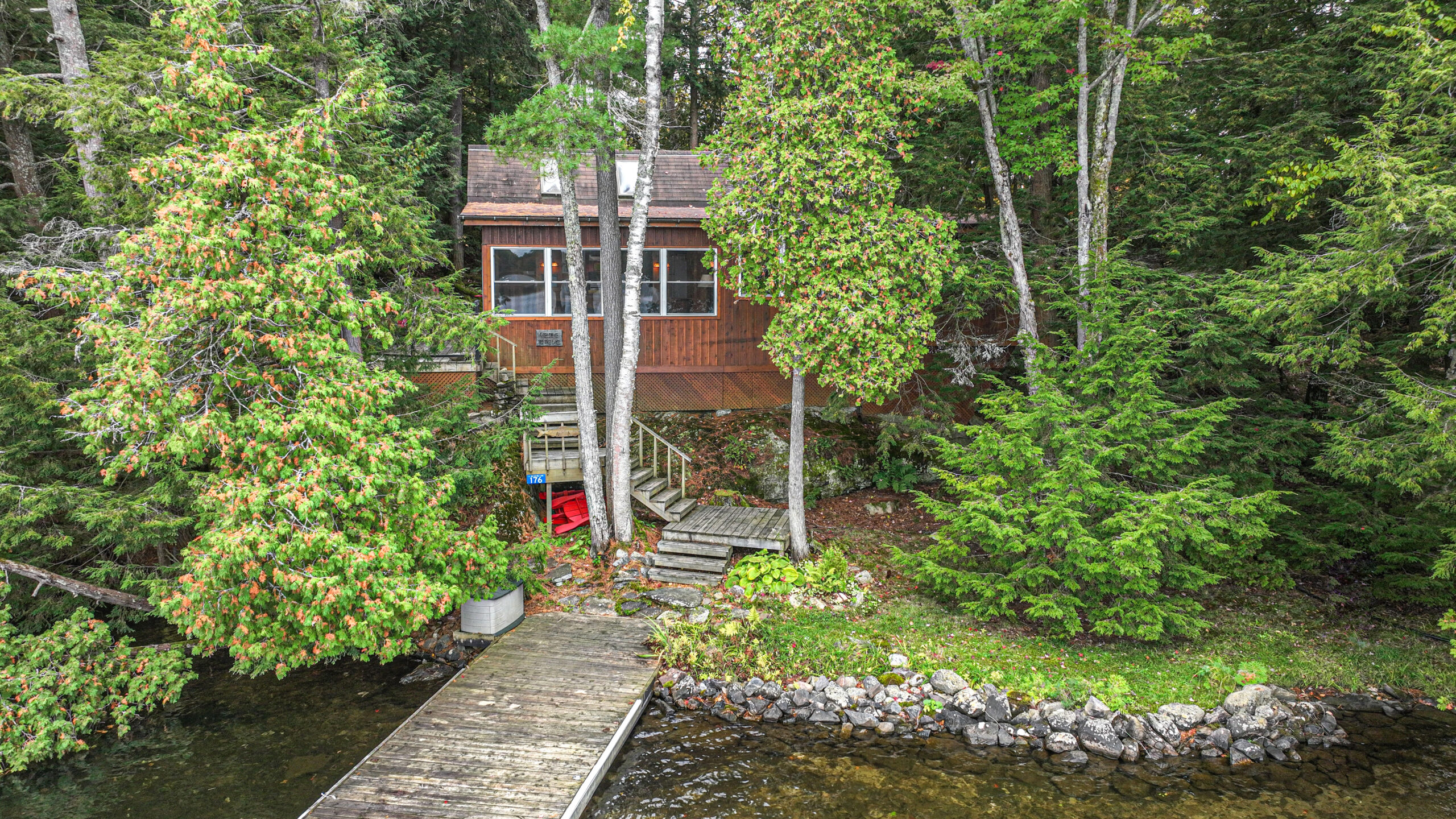 Aerial view of the back of the wooden cottage in the woods with a long dock