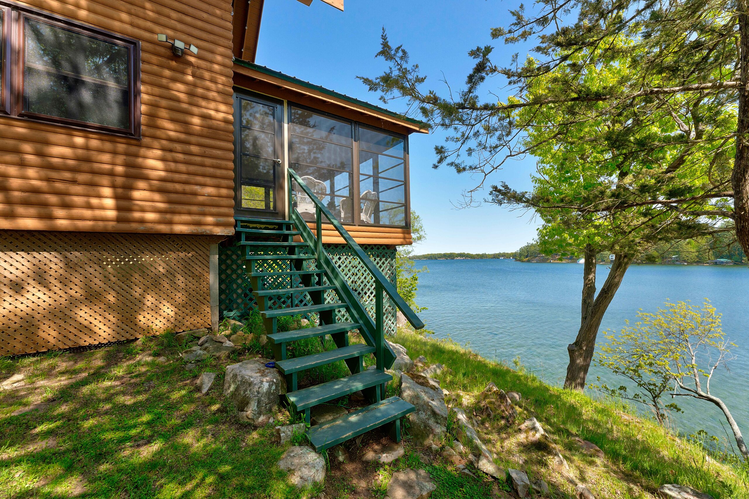 The side of the cottage with green steps and a glass room overlooking the water