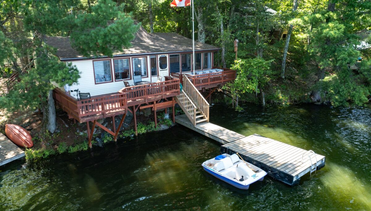 A white cottage with a red deck and a dock on the lake