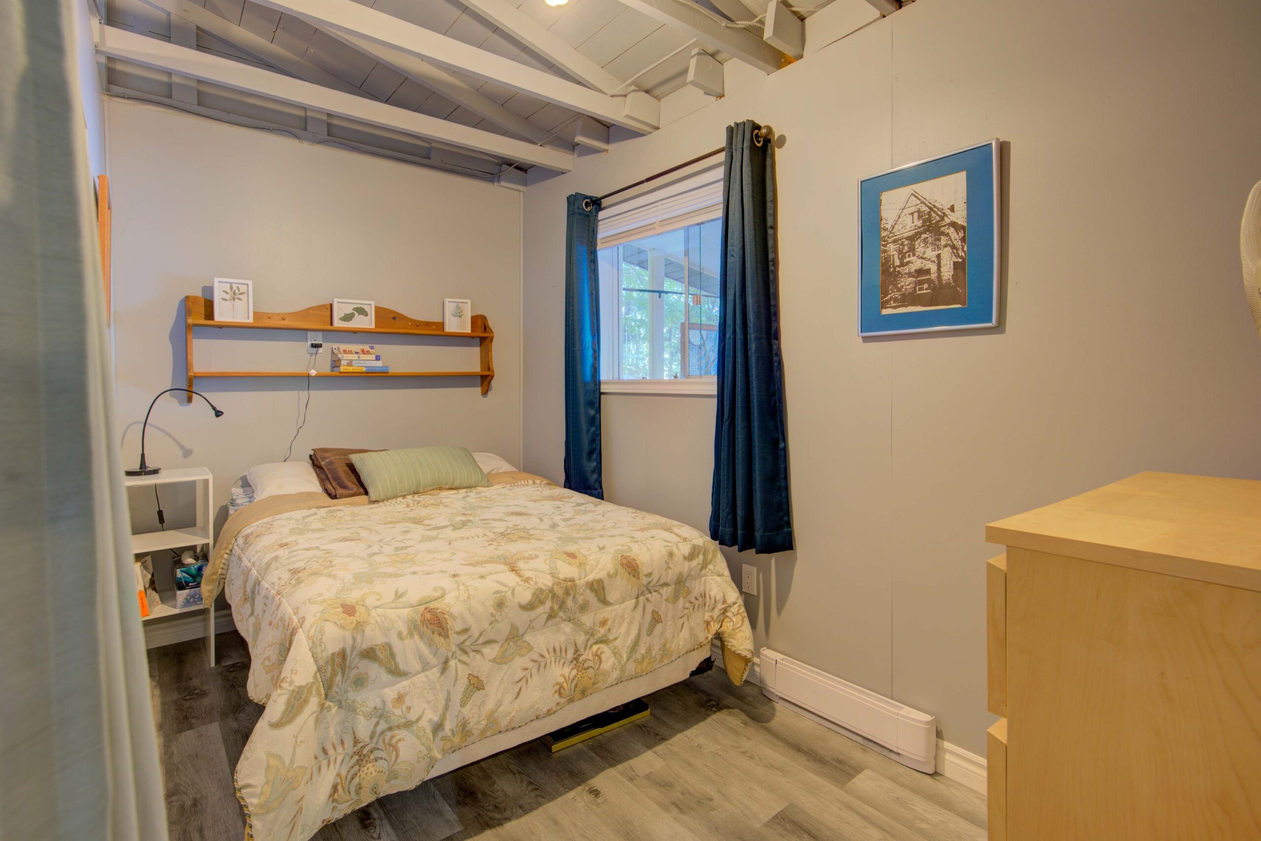 A large bed beside a small window with blue curtains