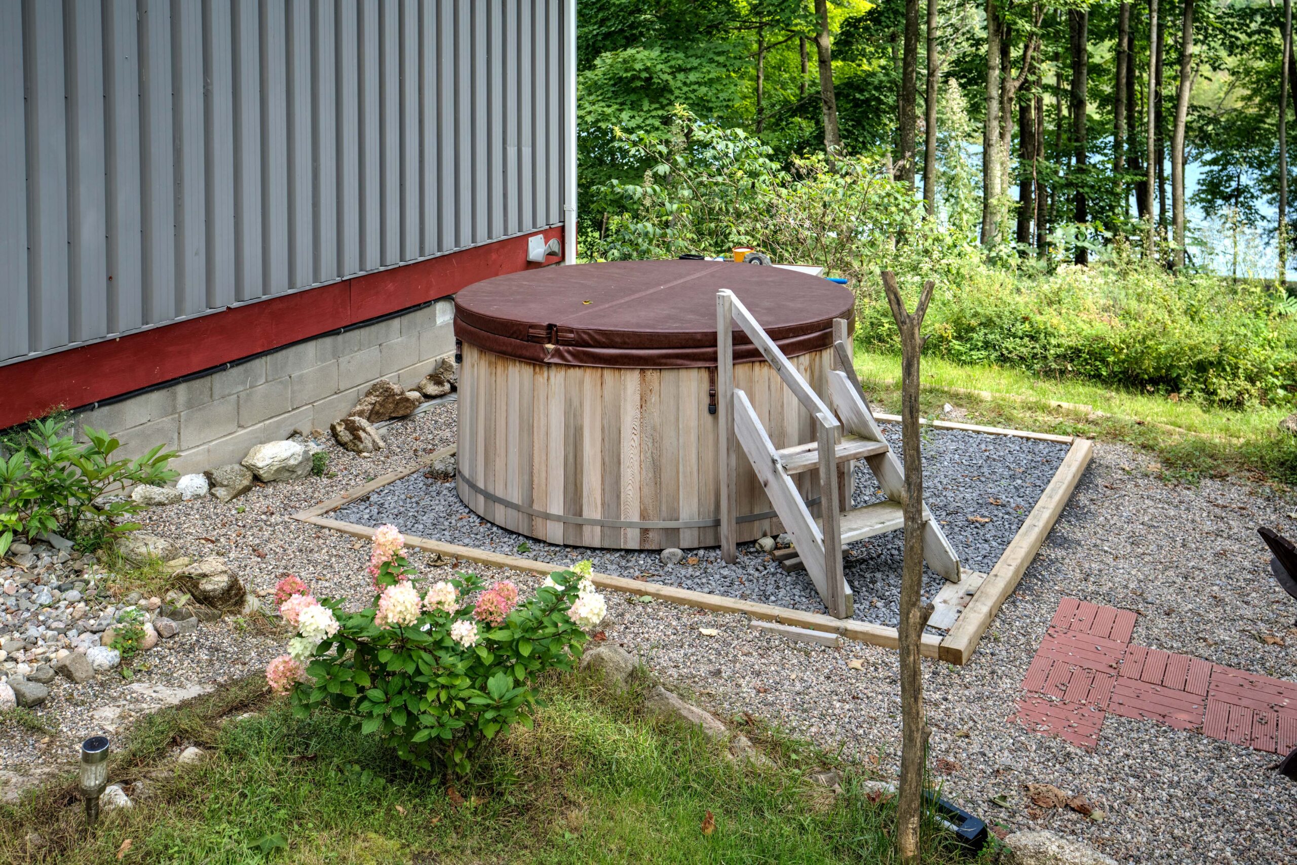 A barrel hot tub on gravel with a hydrangea bush beside