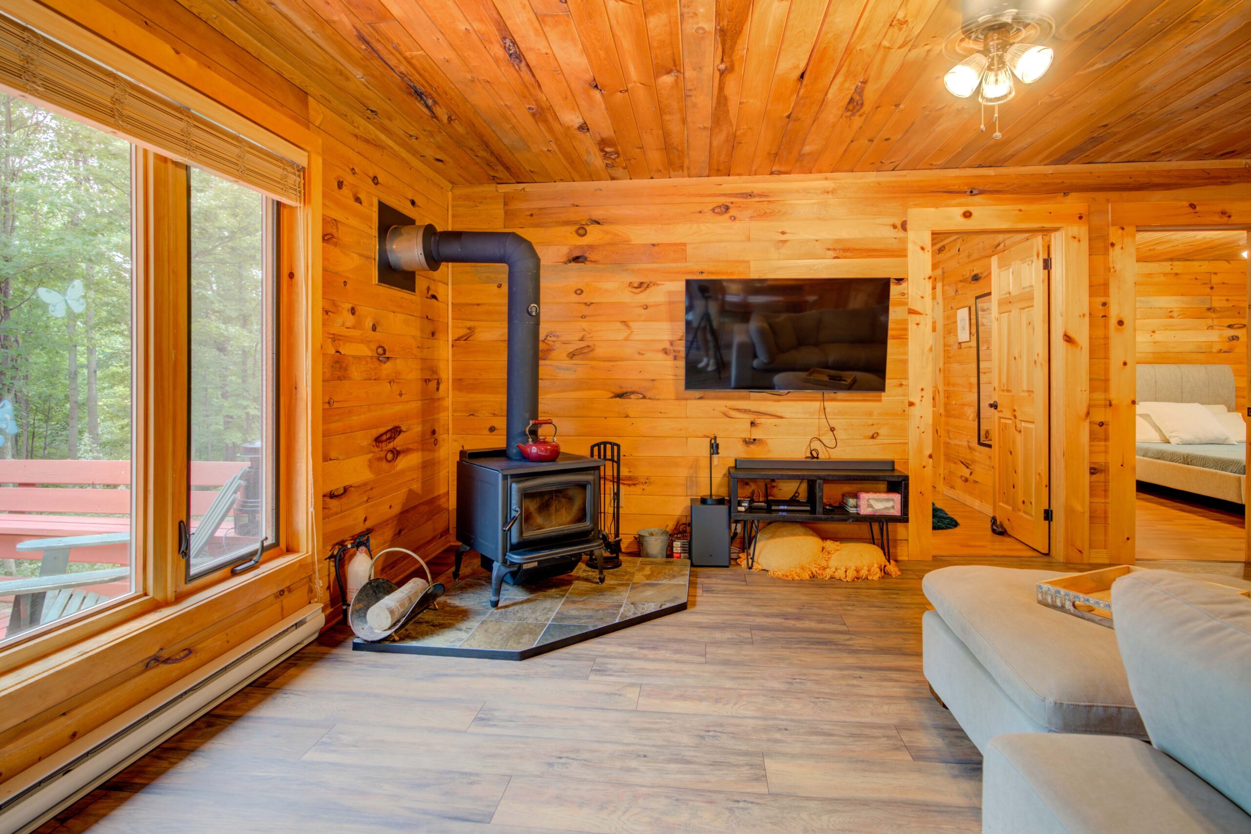 In the corner of a wood-panelled room with a large window, a classic wood stove