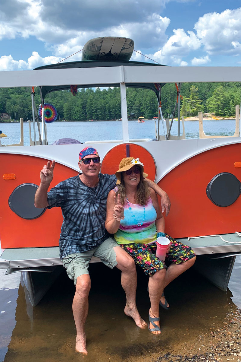 a man and a woman dressed in colourful clothing on the back of a boat decorated to look like a VW van