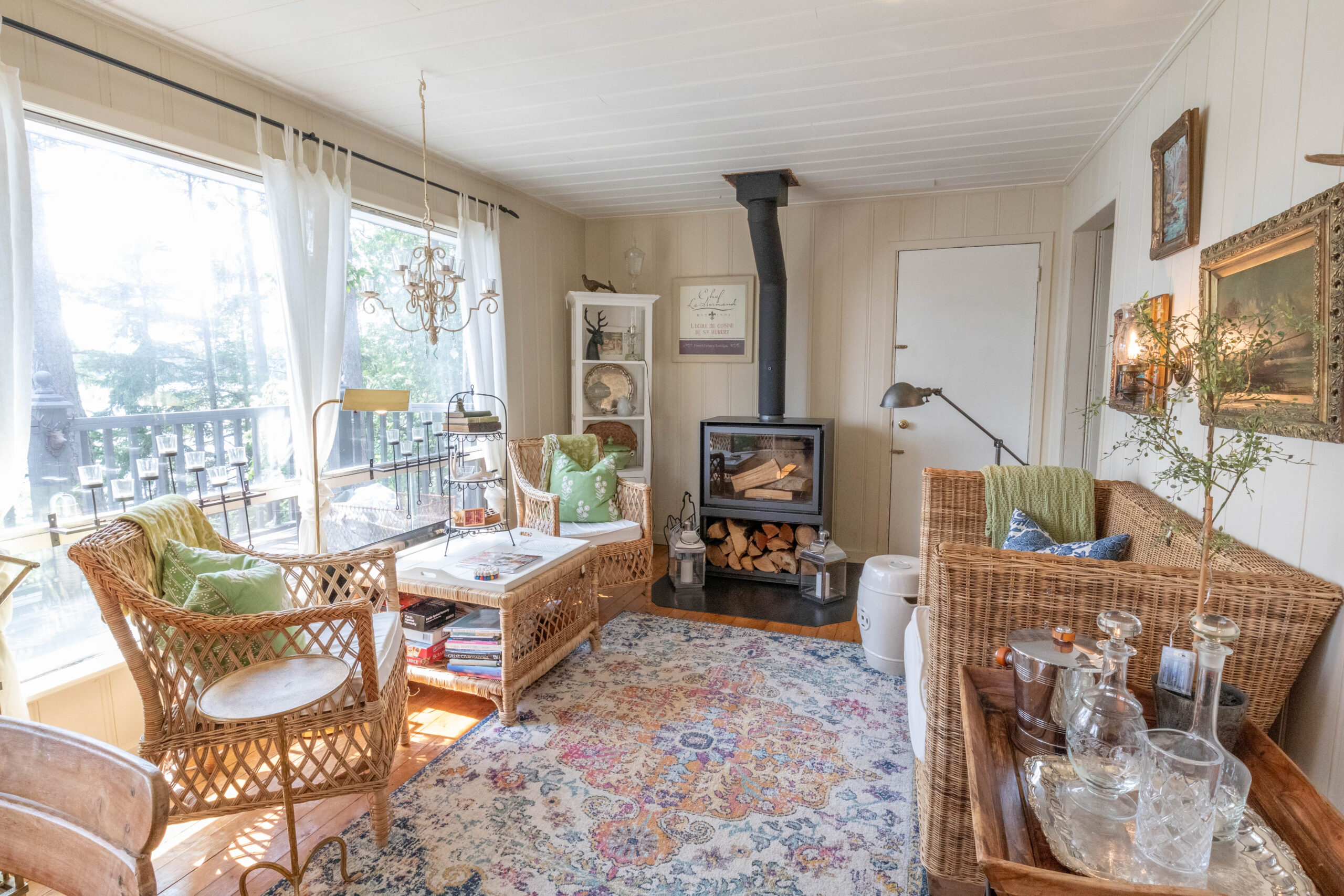 A quaint beige room with a wood stove, large windows, huge patterned carpet and seating areas