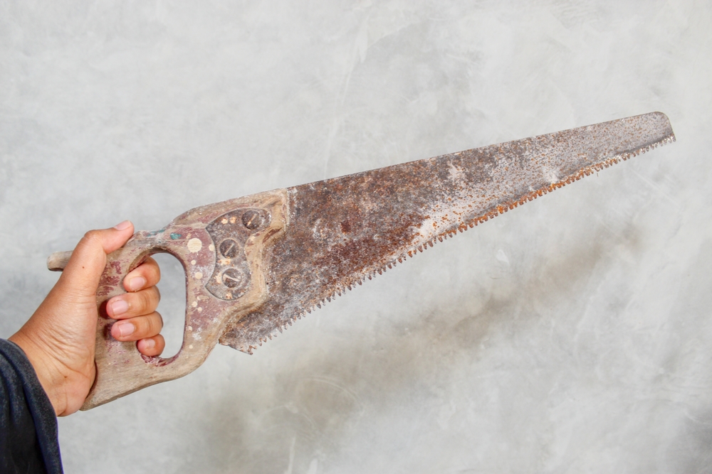 A hand holding a rusty saw against a grey background.