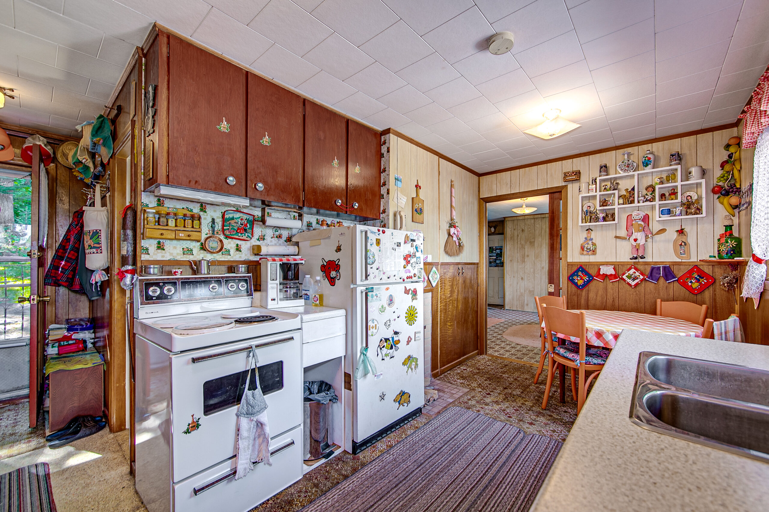A small kitchen with a purple carpet, white appliances, and brown cabinets