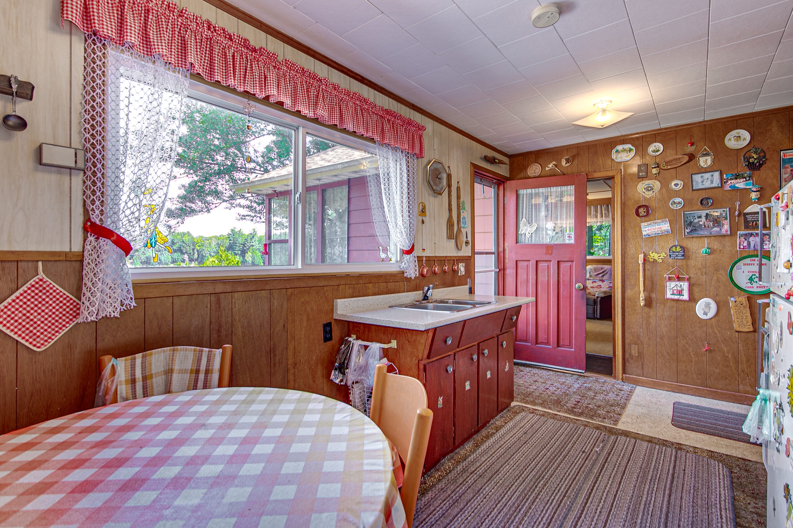 A round dining table with a red and white checkered tablecloth in a small kitchen