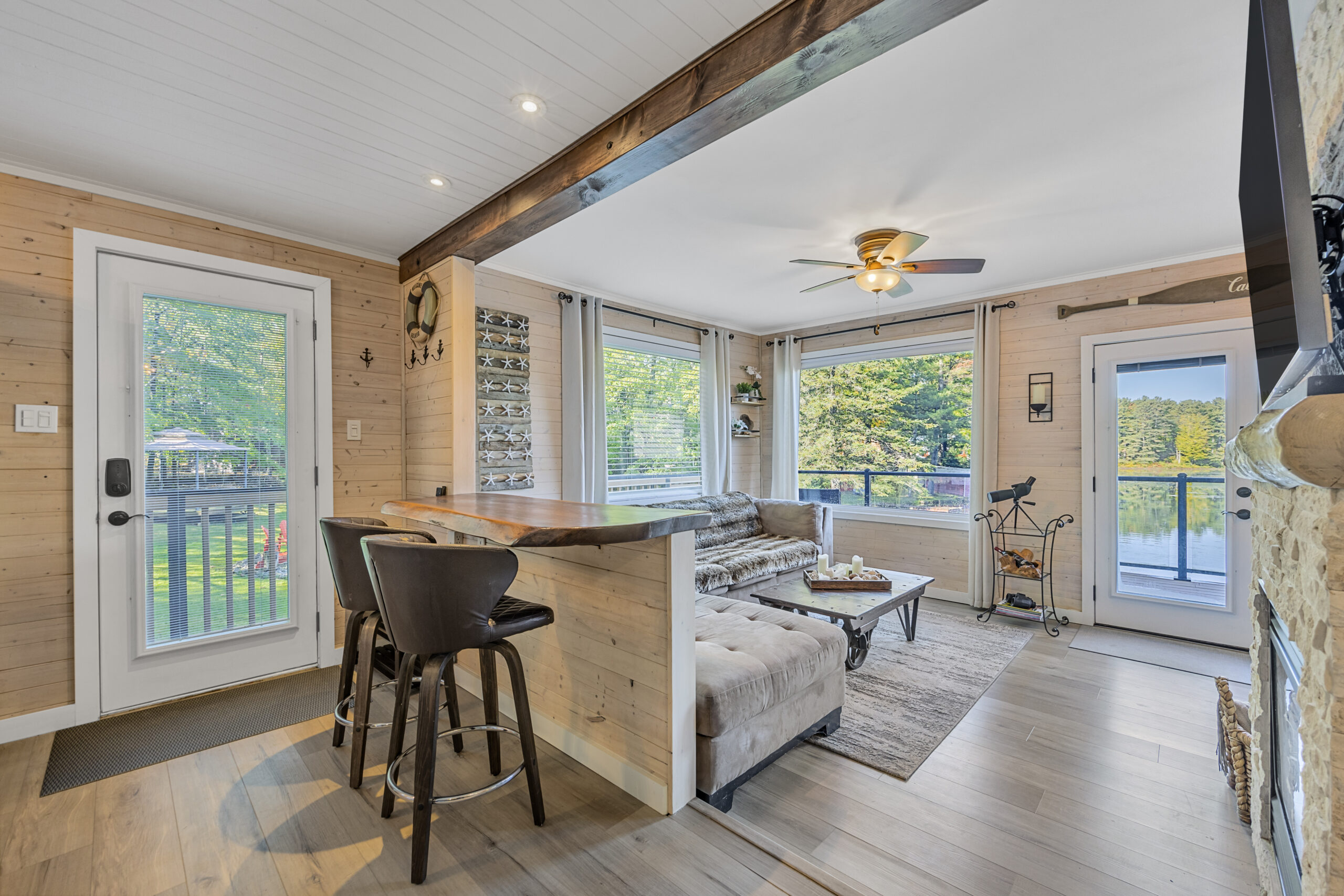 Two grey bar stools face a high top table. In the connecting room, an L-shaped grey couch