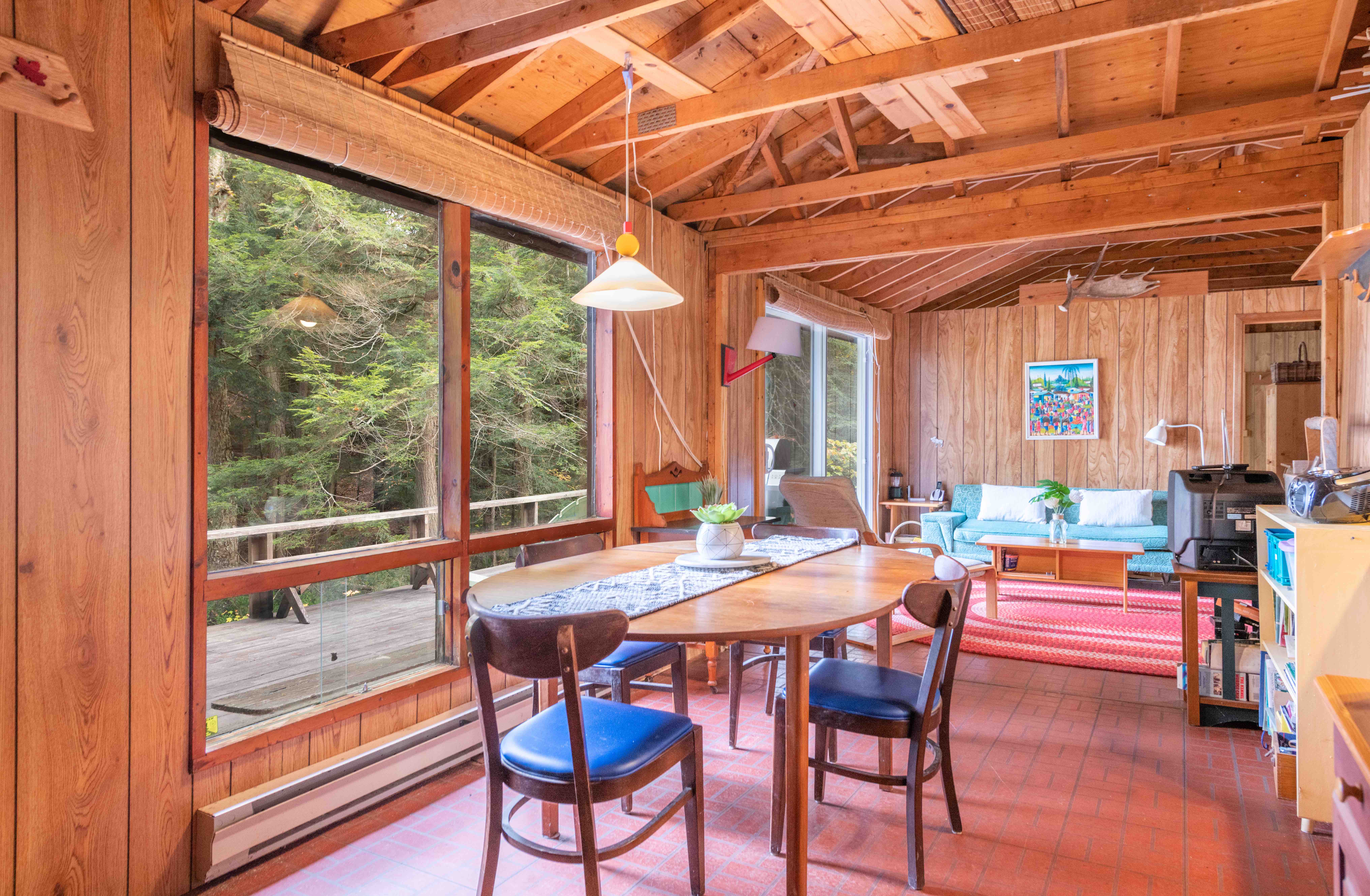 A round wood table with blue chairs around it faces a large window
