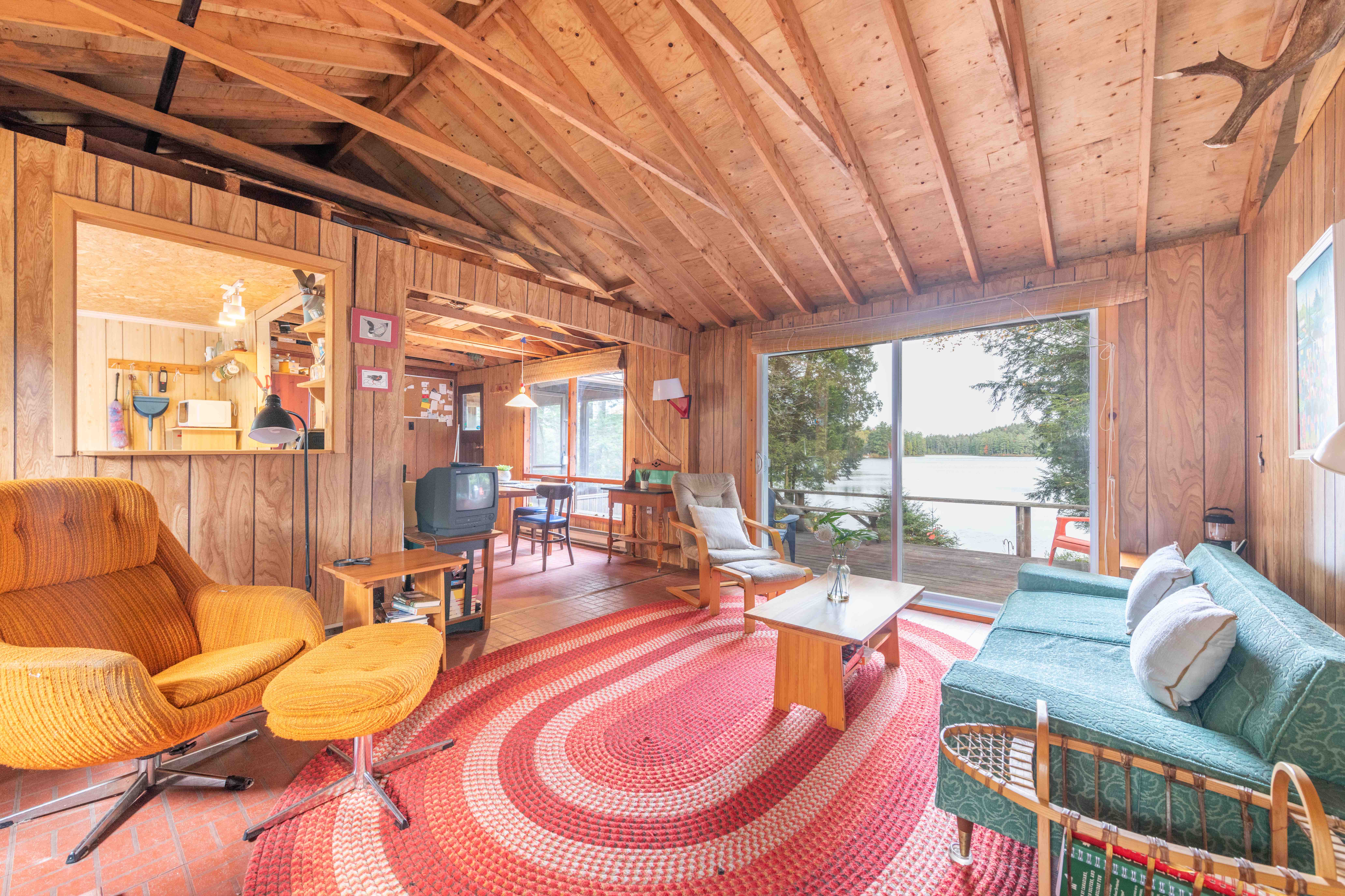 A wood living room with vaulted ceilings and a large round red carpet. A large window offers lake views