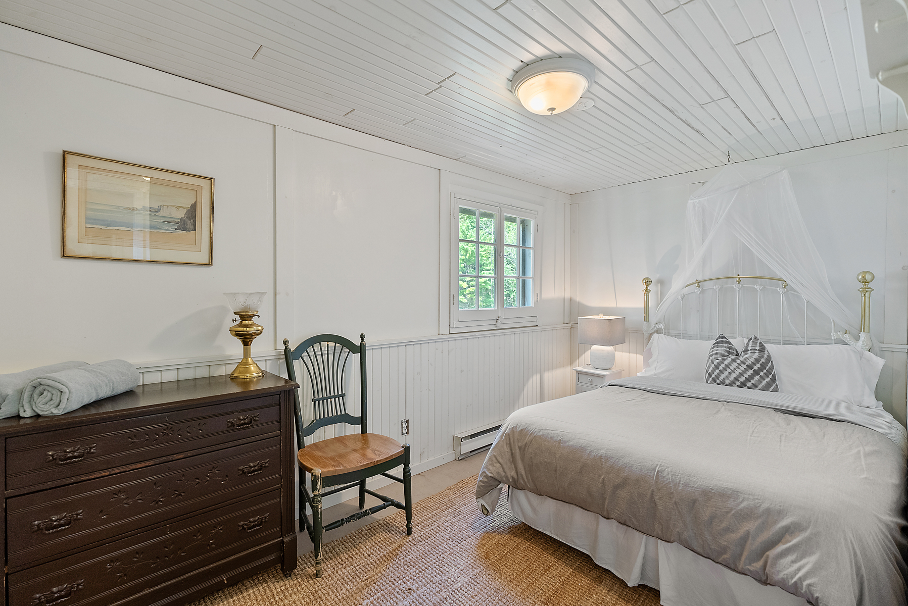 A large beige bed in a white room with a dark wood dresser