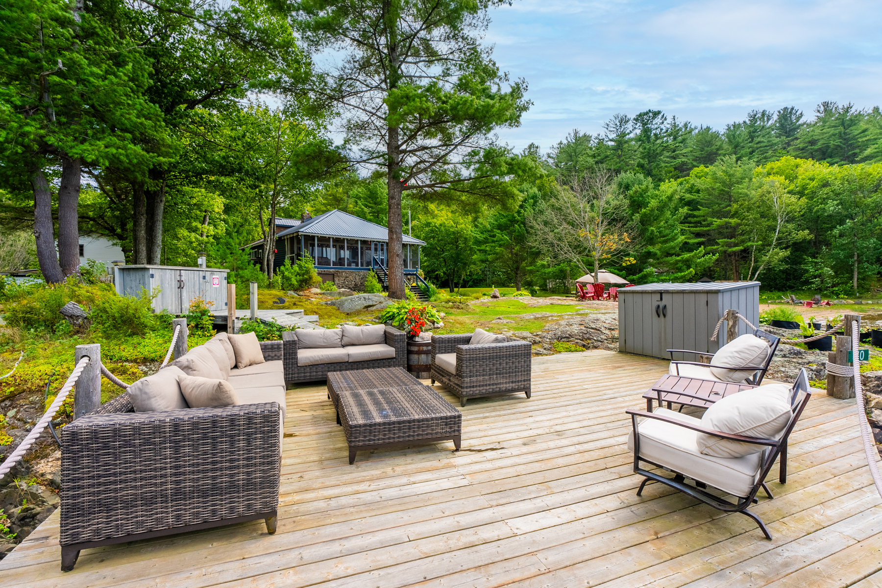 Patio furniture on a lakeside dock with the blue cottage in the distance