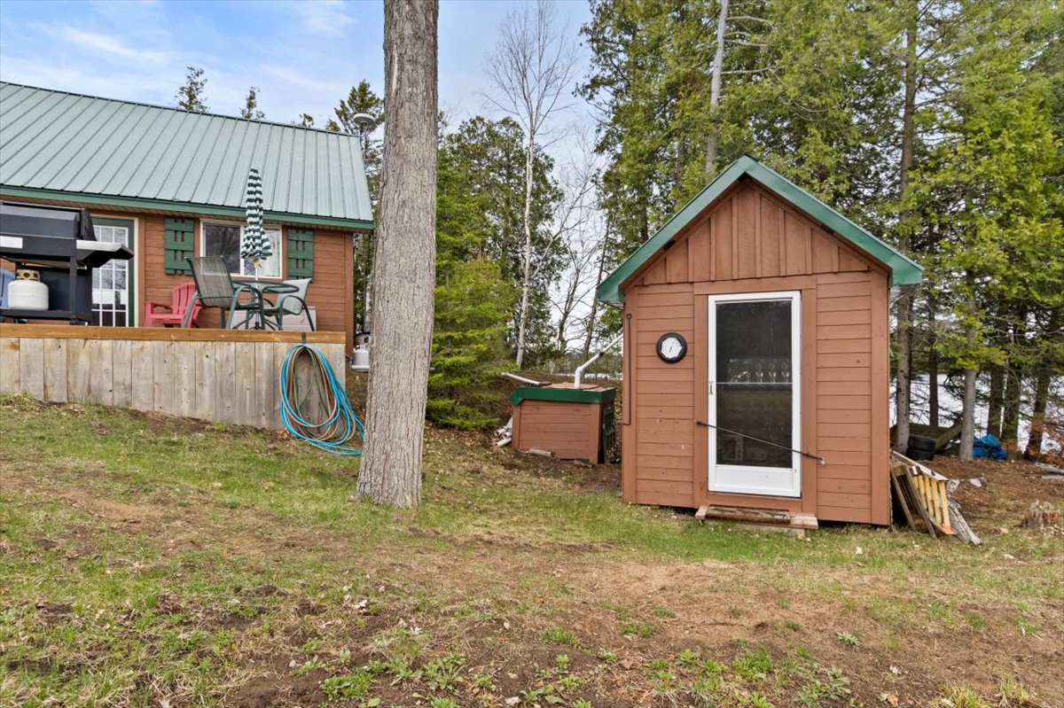 A log cabin with a green roof on a grassy lawn next to a small shed