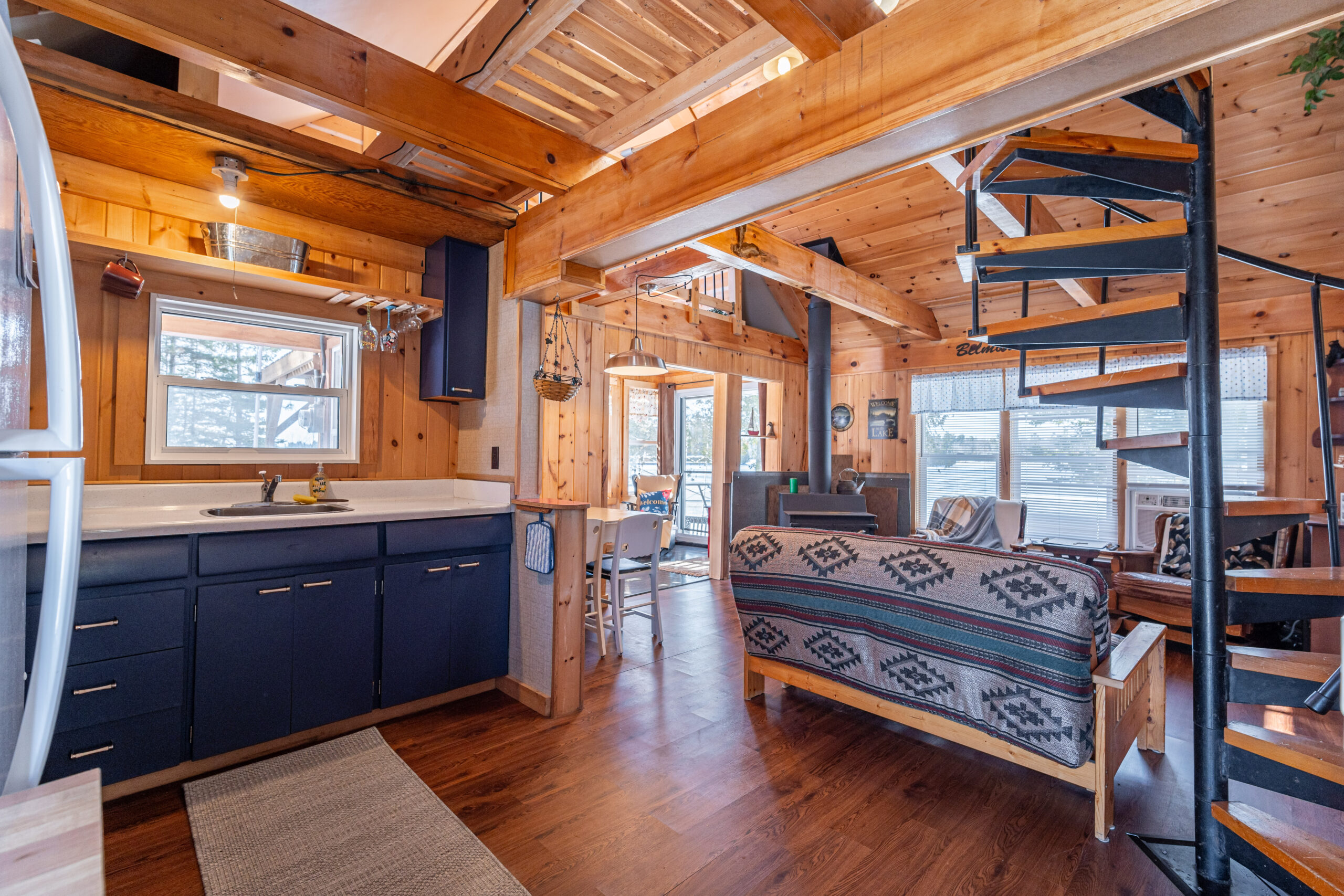 A small kitchen with blue cabinets faces an open-concept living room in a log cabin