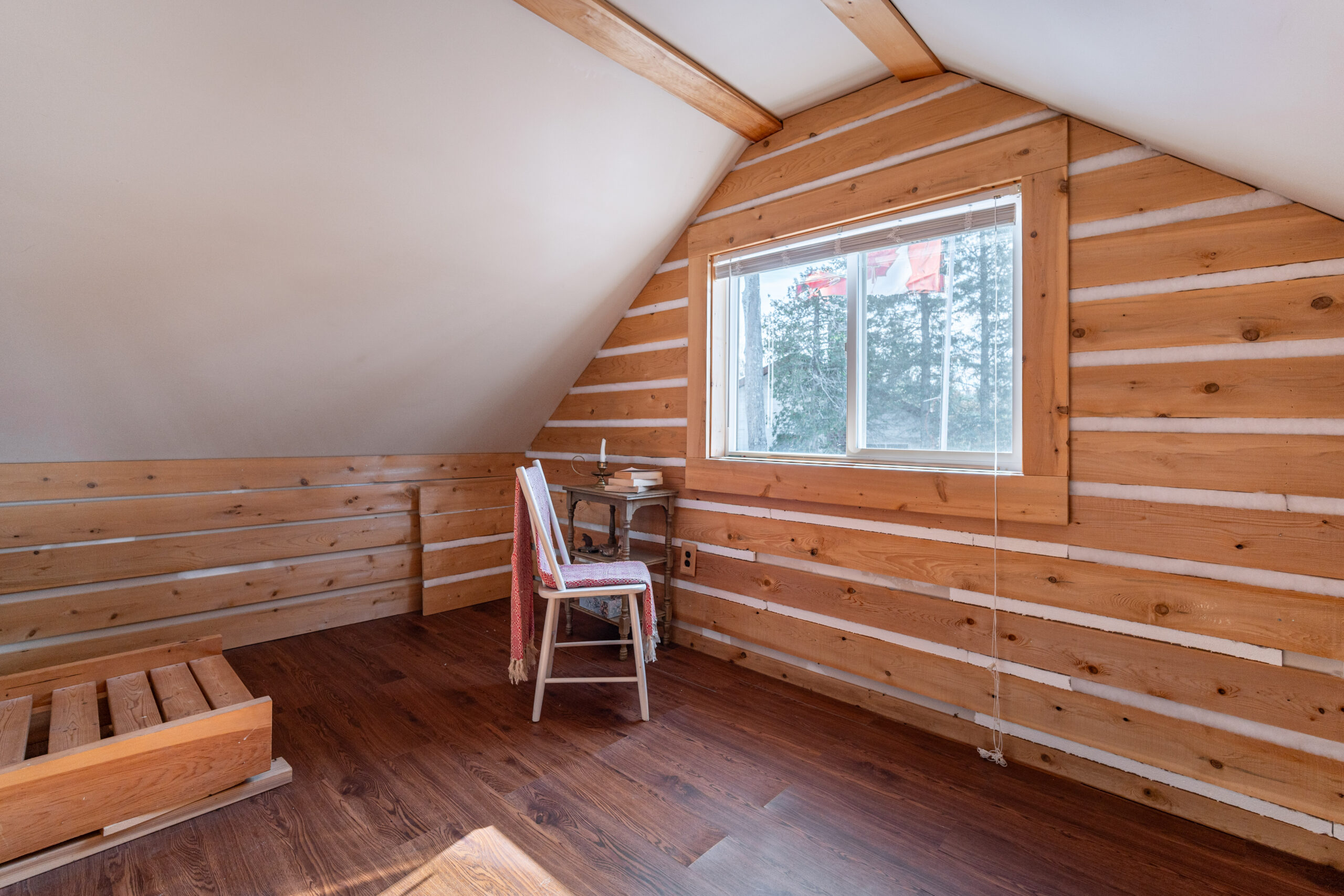 A small white chair faces a window in a log room