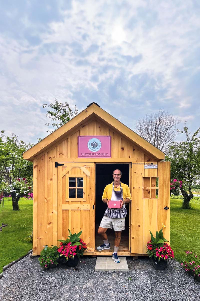 a photo of a man holding a box of butter tarts and standing outside of a shed