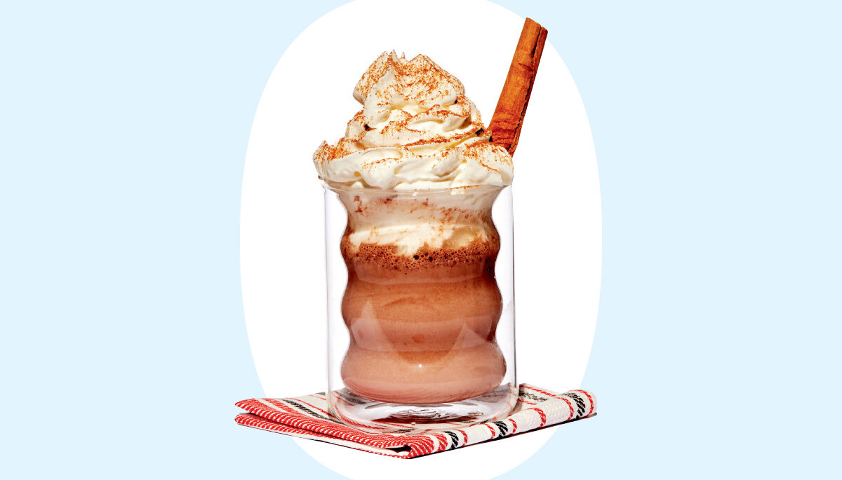 a photo of a creamy drink topped with whipped cream and a cinnamon stick in a glass mug