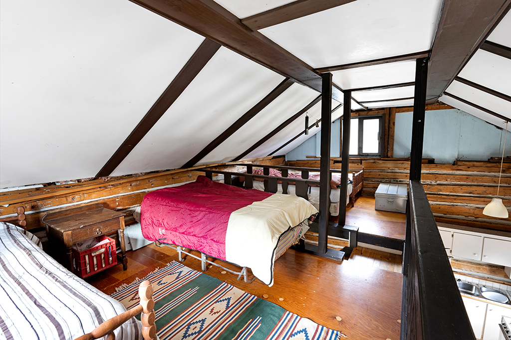 A bed with a red duvet in an attic room with a white ceiling