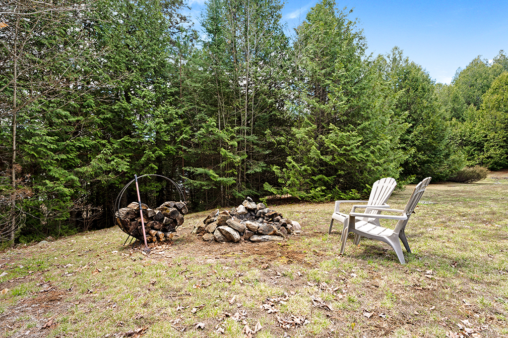 A small fire pit area with two Muskoka chairs on a lawn