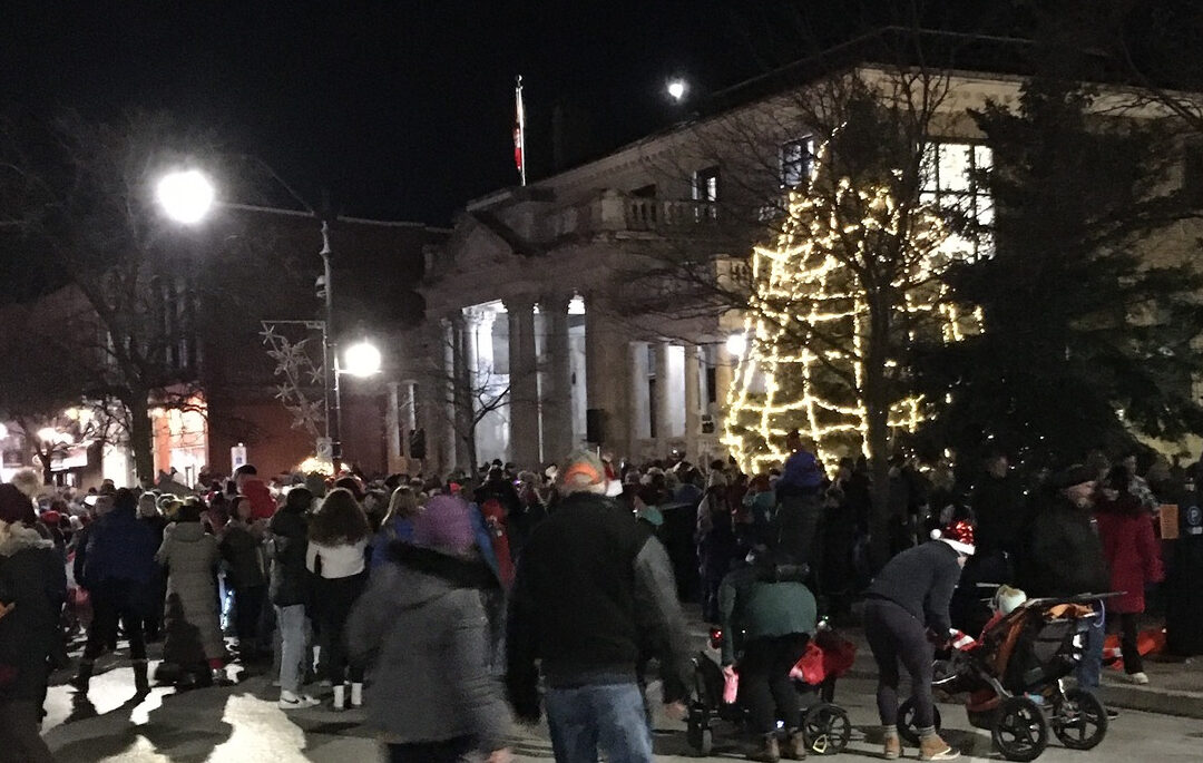 a lit-up christmas tree with folks gathered around