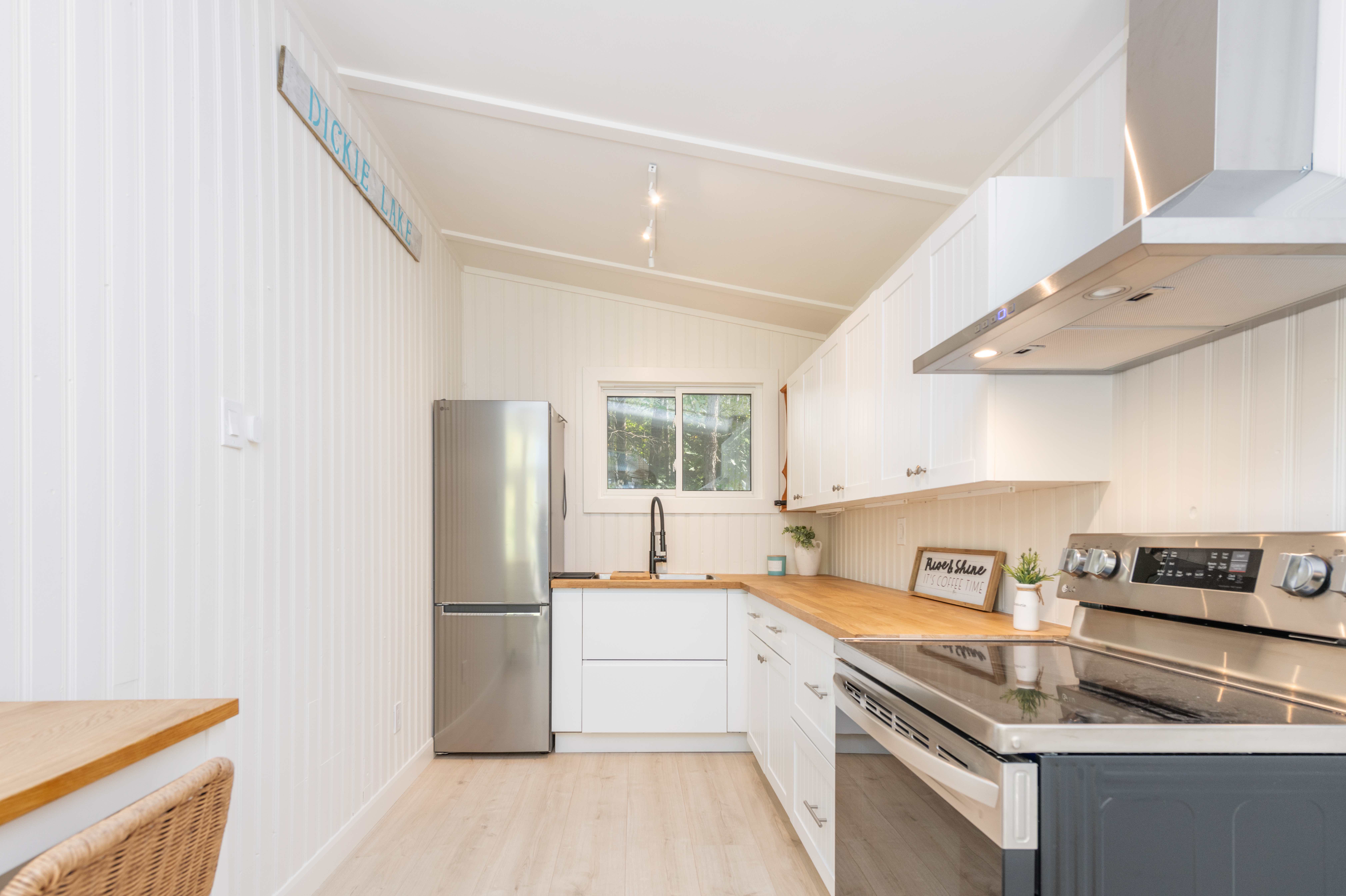An L-shaped kitchen with stainless steel appliances, white cabinets, and a wood countertop