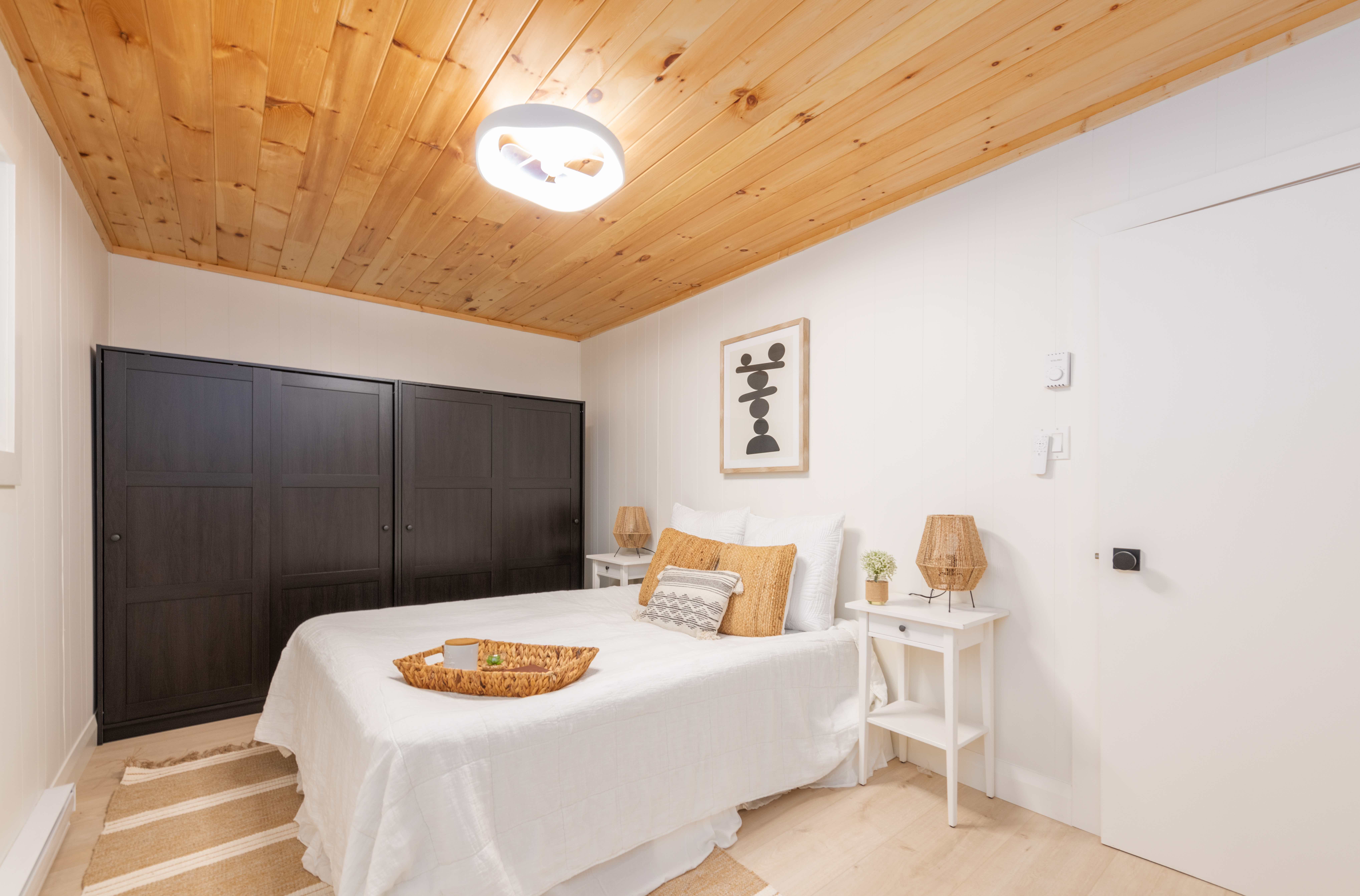 A white bed in a white room with a wood ceiling