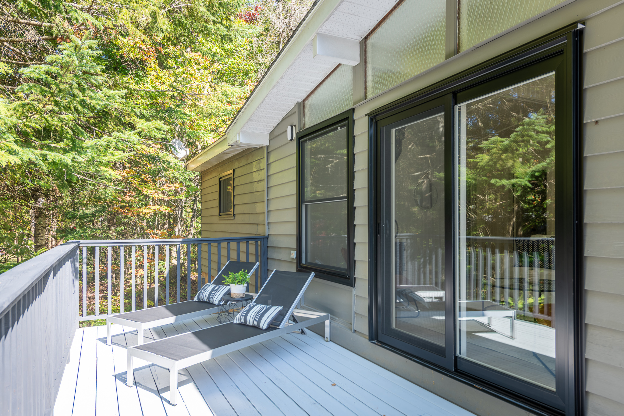 Black lounge chairs on a deck next to a paneled cottage with a bright sliding door