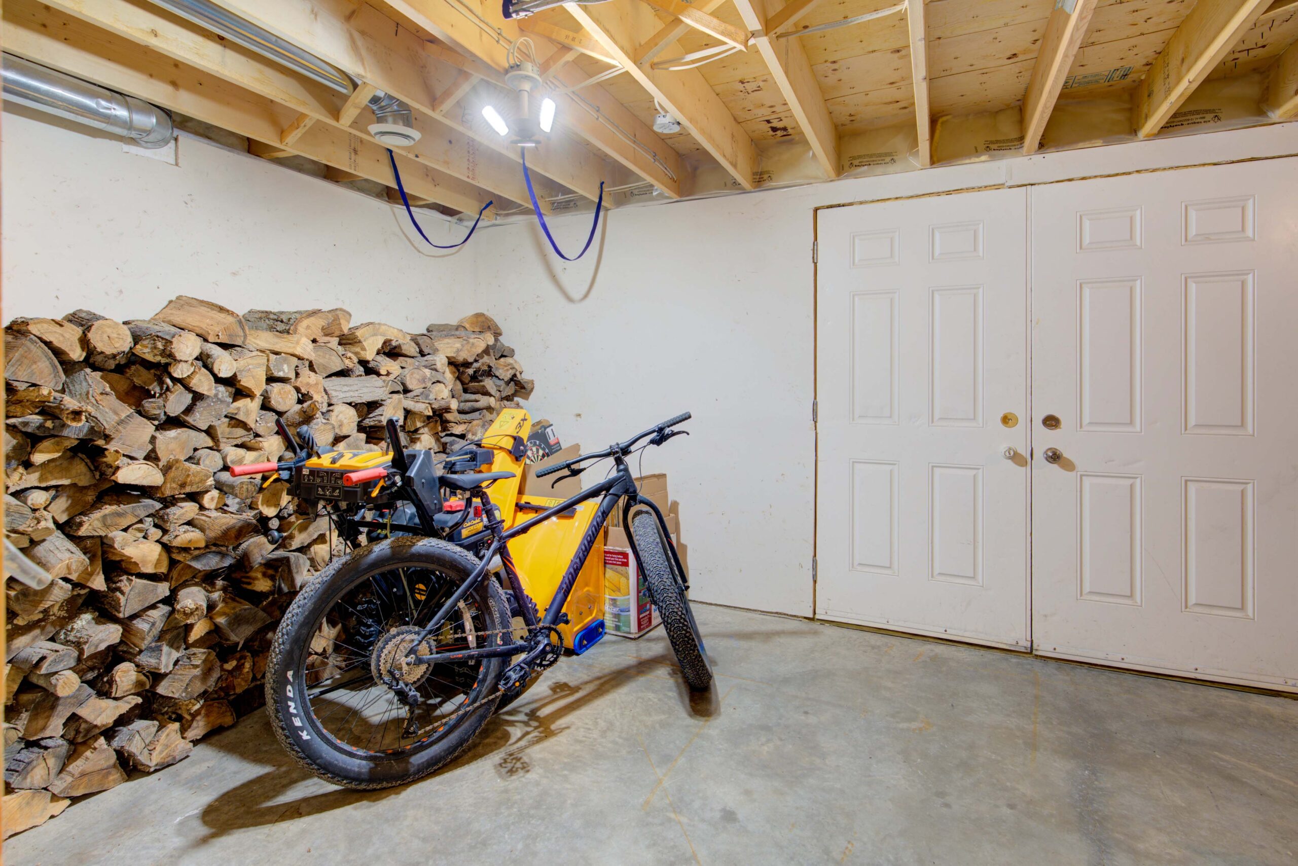 A yellow and black dirt bike leans against a stack of logs in a white room