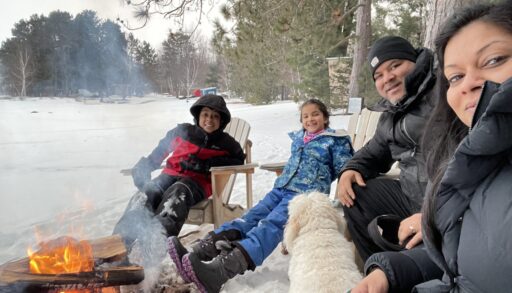 a family of four sit around a campfire in winter
