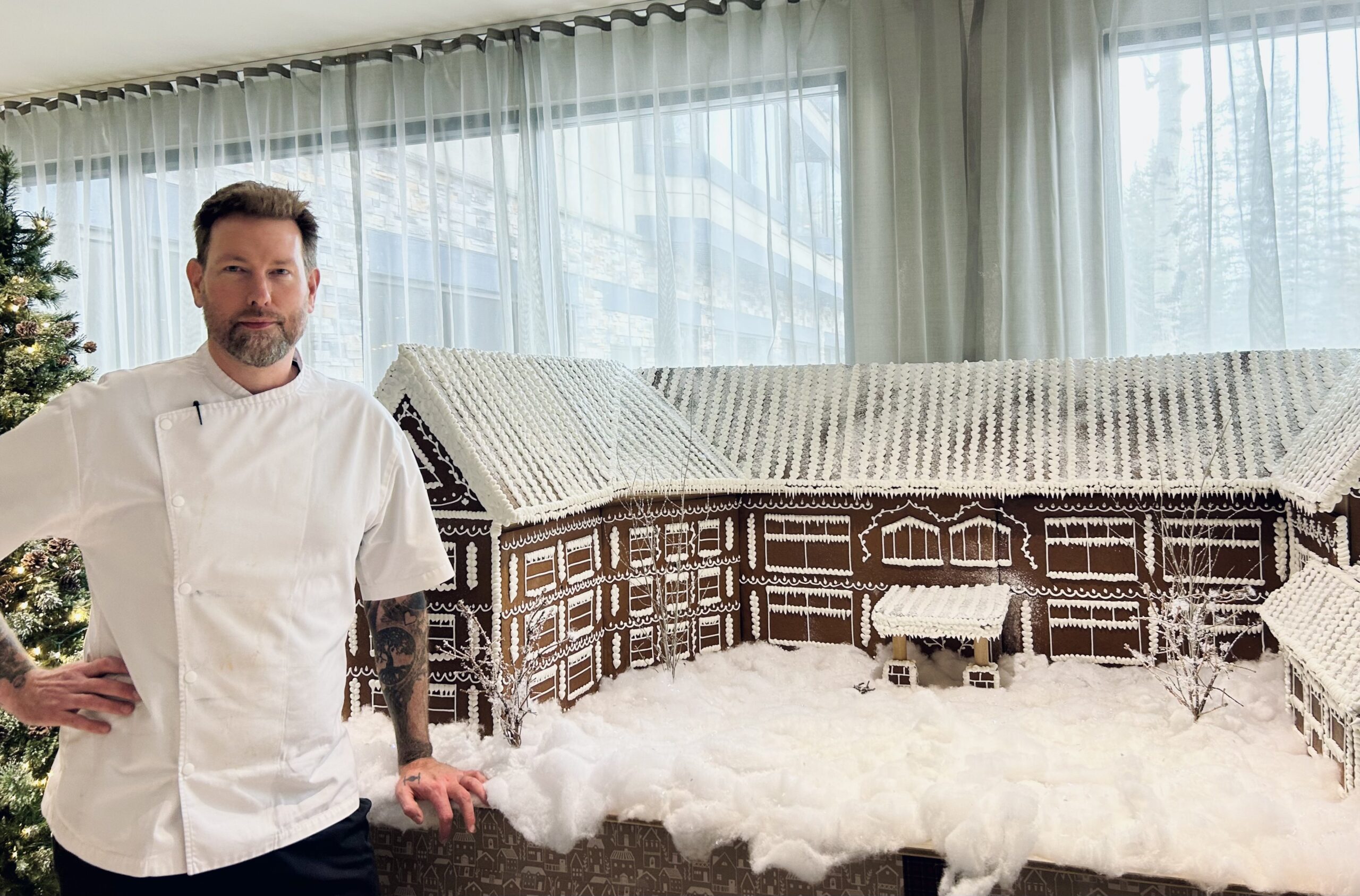 A chef poses beside a huge gingerbread house
