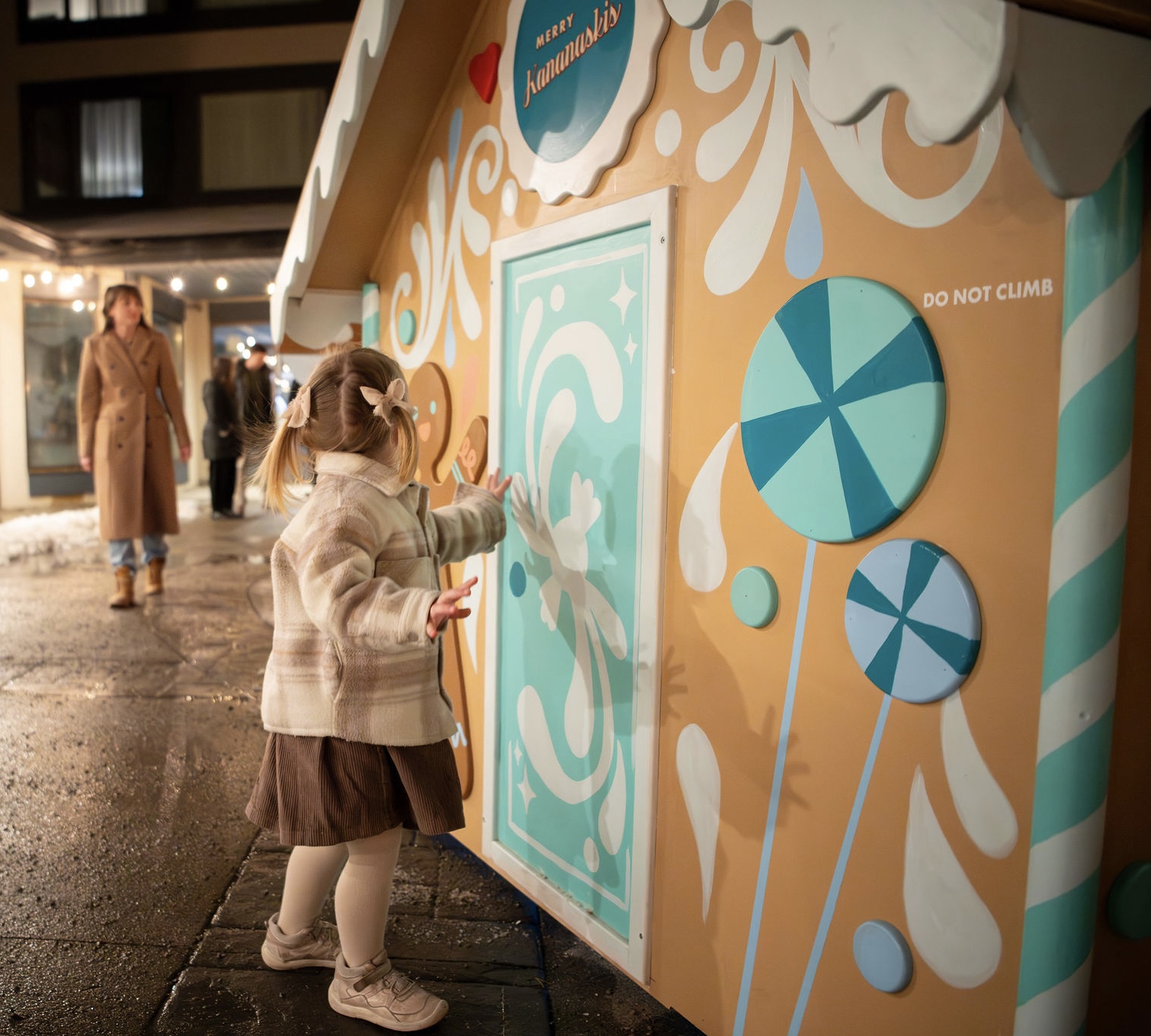 A little girl knocks on the blue door of a fake gingerbread house