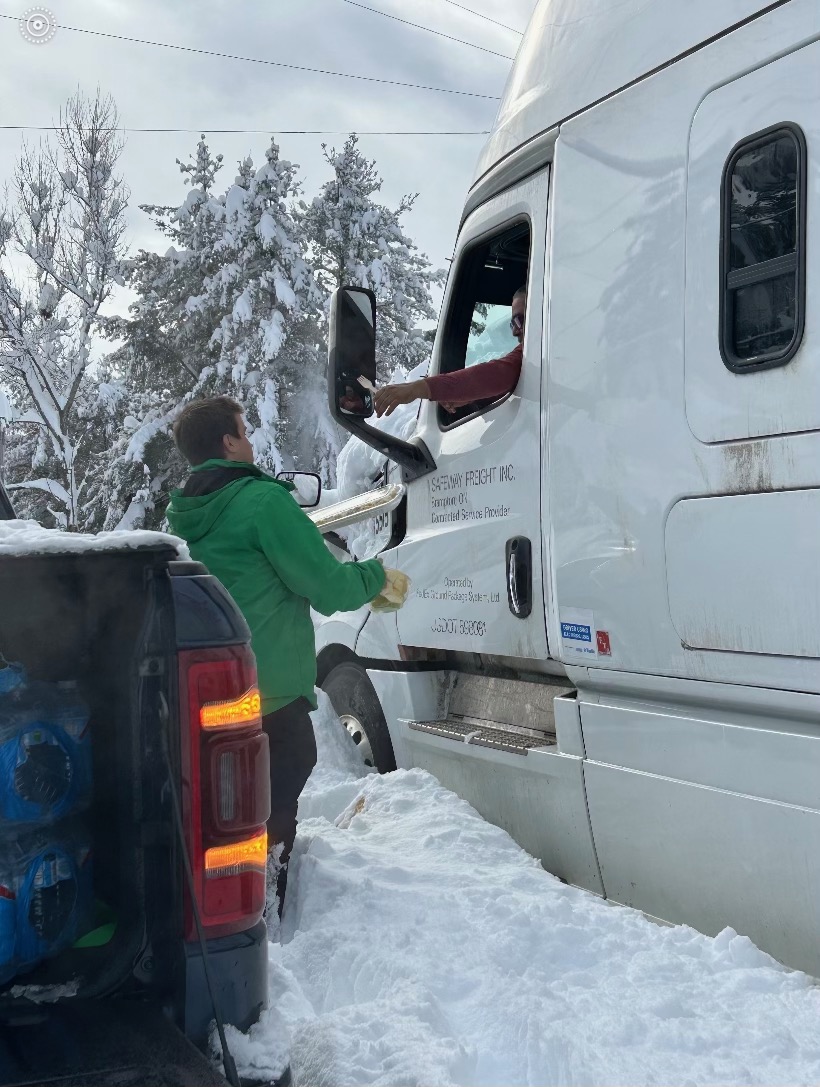 a man in a green jacket stands outside of a truck in the snow