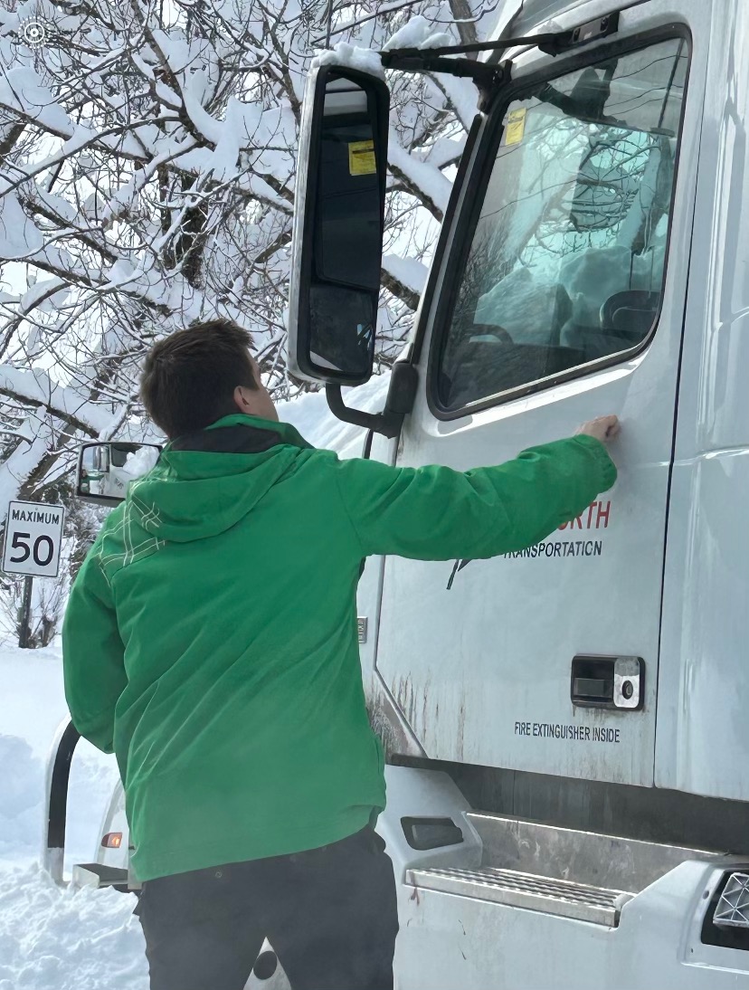 a man in a green jacket stands outside of a truck in the snow