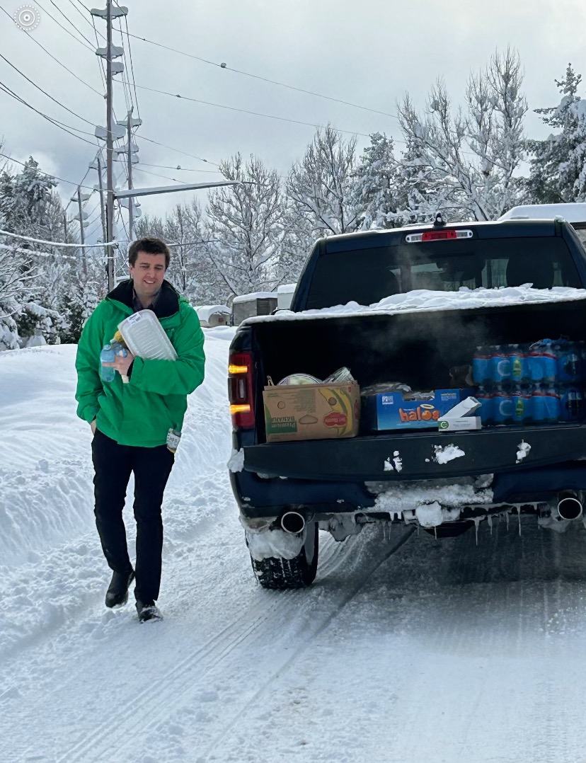 a man in a green jacket stands outside of a truck in the snow