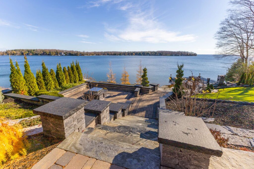 A spacious stone patio leads down to a blue lake