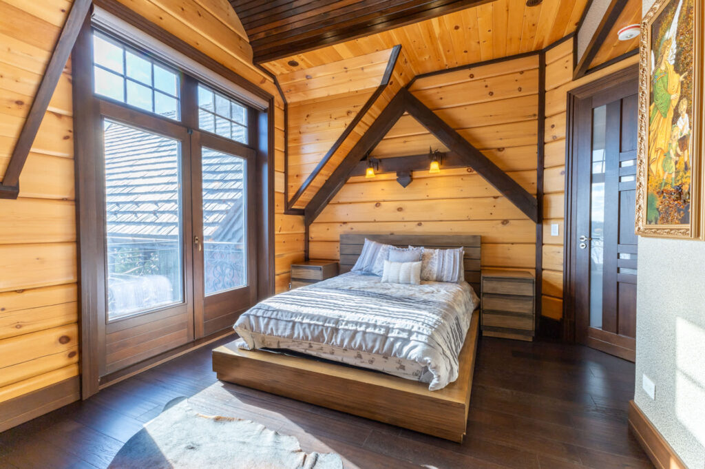 A white bed on a wood bed frame beside a large window