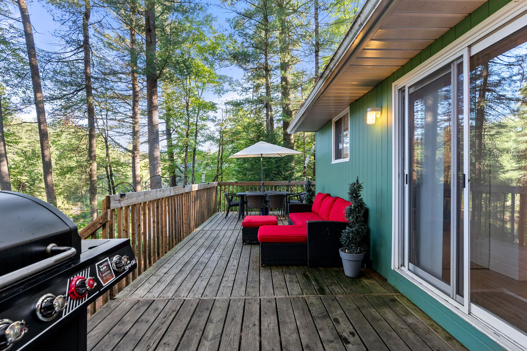 A red couch faces the railing. At the other end, a small outdoor dining set