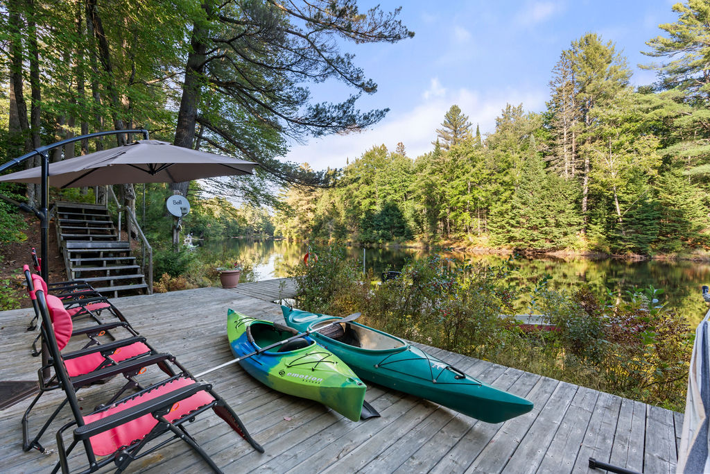 A wood dock with two green kayaks and red chairs sit on the dock