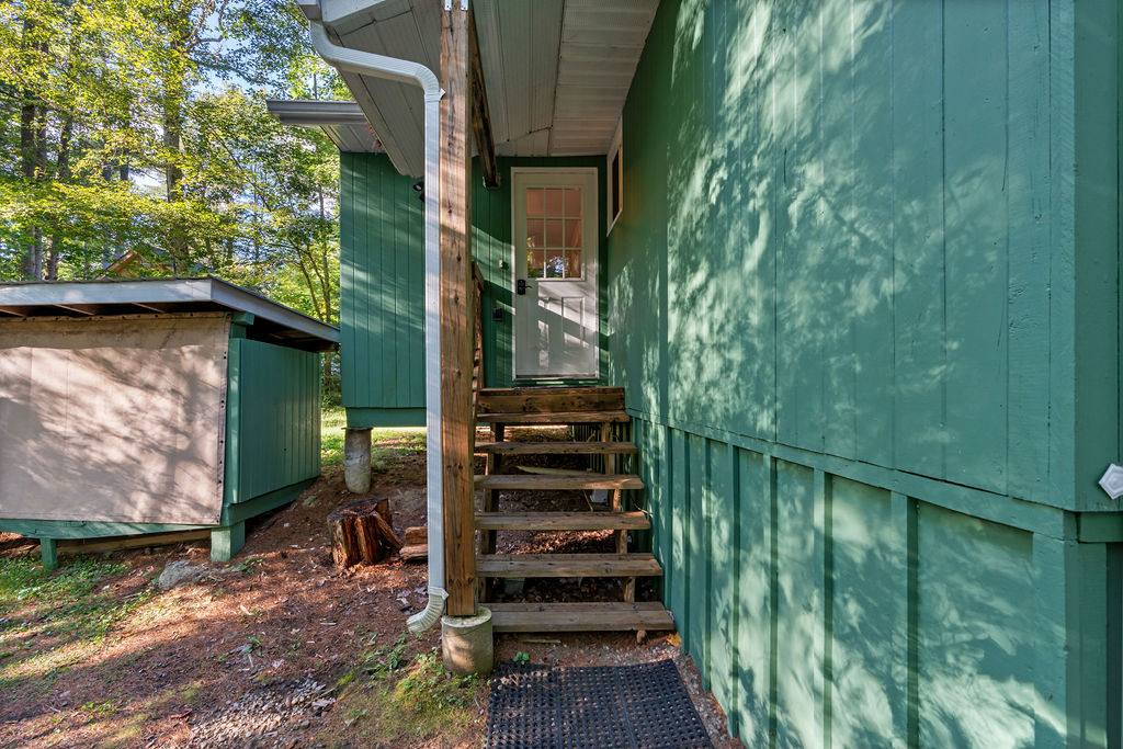 Wood steps lead up to a narrow front porch of a green paneled cottage