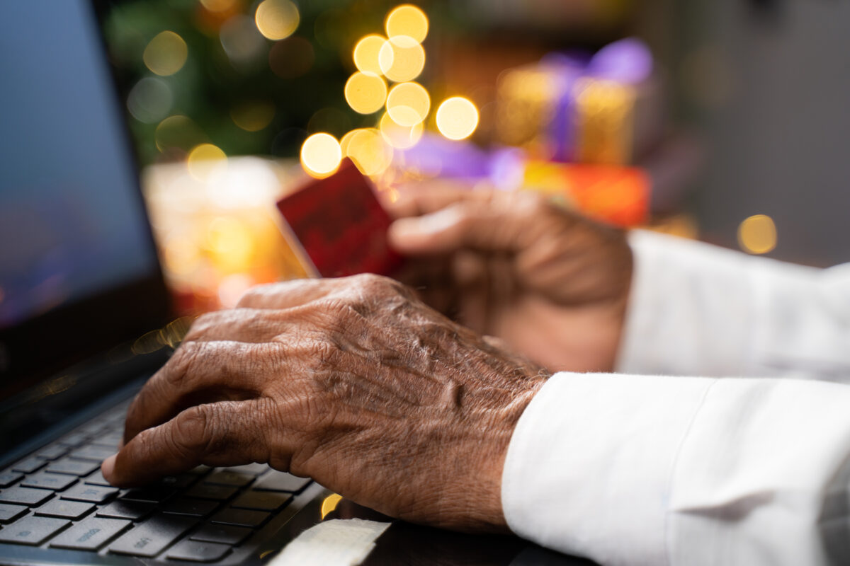 a photo of a person's hands typing on a computer while holding a credit card with holiday lights in the background