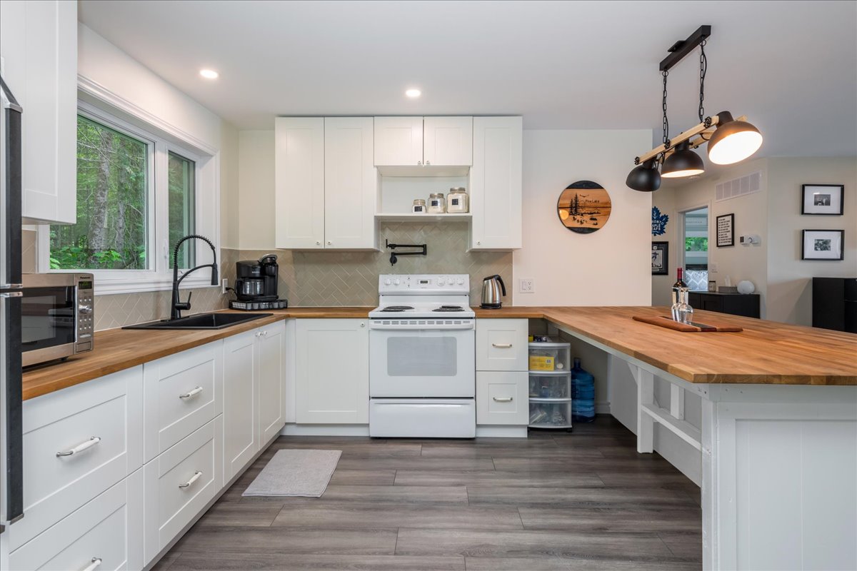 A bright white kitchen with grey hardwood floors and brown wood countertops