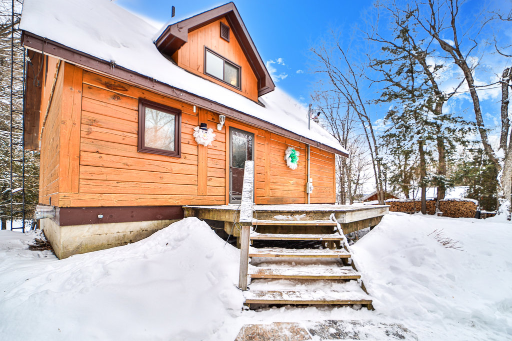 Wood steps lead up to a A red-brown cottage with black trim in the snow